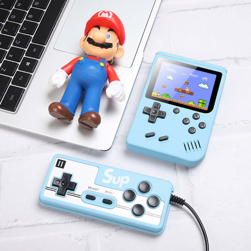 Retro Mini Handheld Game Console next to a toy figure and a game controller on a desk.