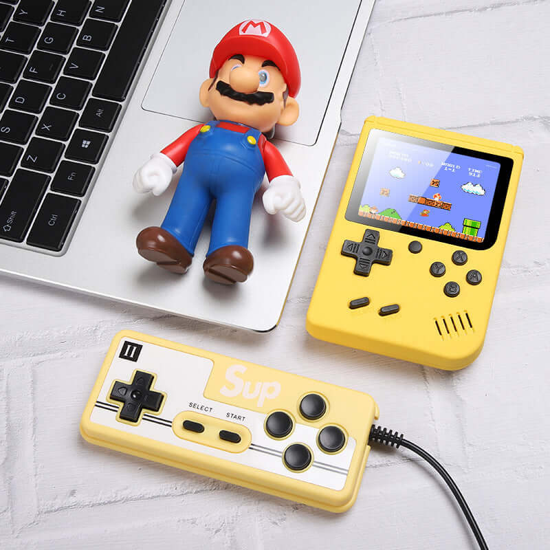 Retro Mini Handheld Game Console on desk with a gaming controller and toy figure