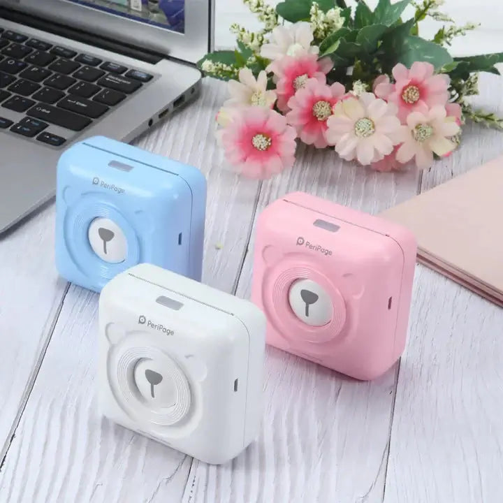 Colorful PeriPage Pocket Printers in blue, white, and pink next to a laptop with flowers in the background, showcasing the compact design.