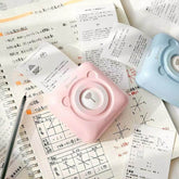 Pink and blue PeriPage Pocket Printer printing notes on a desk with an open notebook and pen nearby.